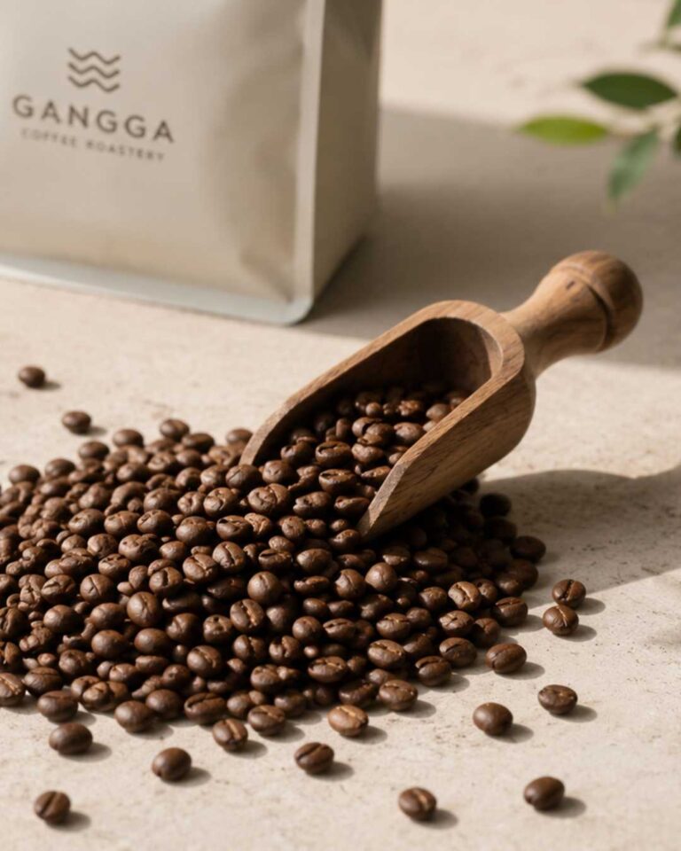Wooden scoop filled with freshly roasted coffee beans beside Gangga Coffee Roastery packaging.