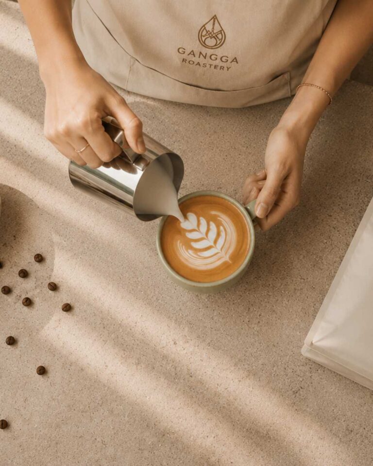 Barista pouring latte art while wearing a Gangga Roastery apron, serving freshly roasted specialty coffee.